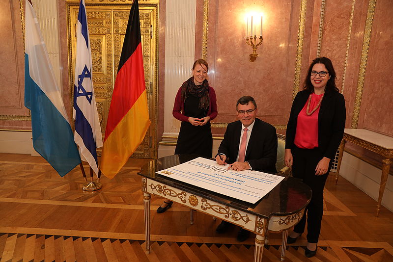 Europaminister Dr. Florian Herrmann, MdL (Mitte) mit der israelischen Generalkonsulin Sandra Simovich (rechts) und Anna Abelmann-Brockmann (links) von der Wissenschaftlichen Koordinierungsstelle Bayern-Israel der Bayerischen Forschungsallianz (BayFOR) beim Unterzeichnen des Förderbescheids